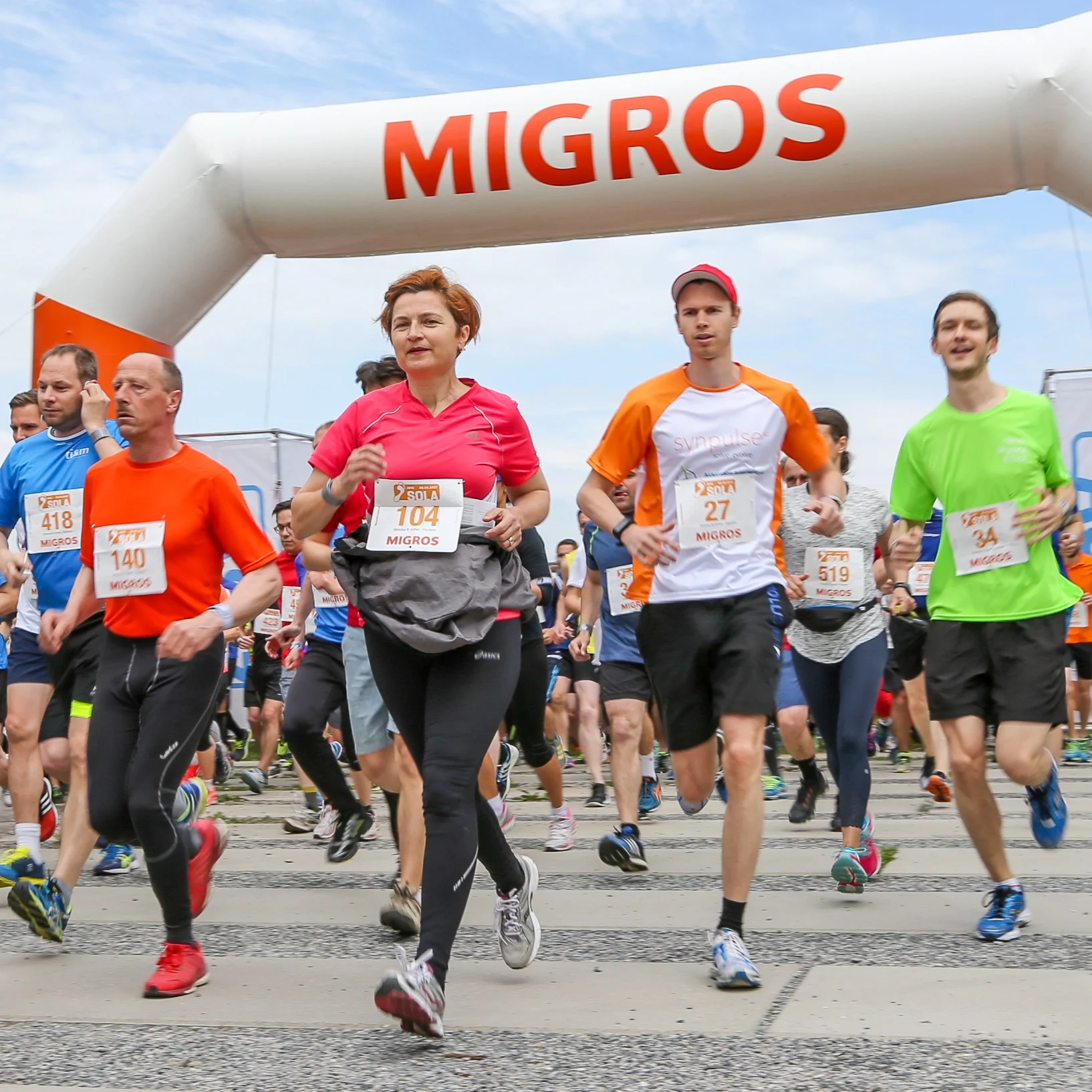 Läuferinnen und Läufer laufen unter einem aufblasbaren Torbogen der Migros.