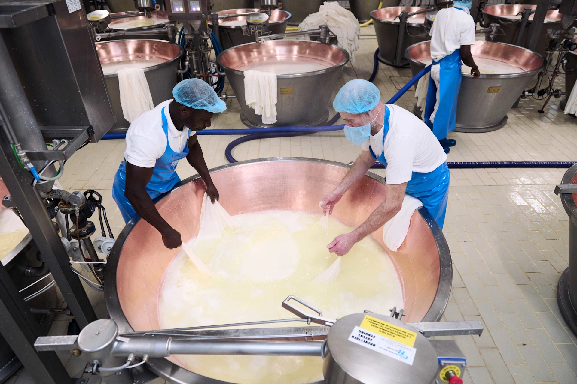 Two men lift the cheese of the vat so that it can drain off and shed whey.