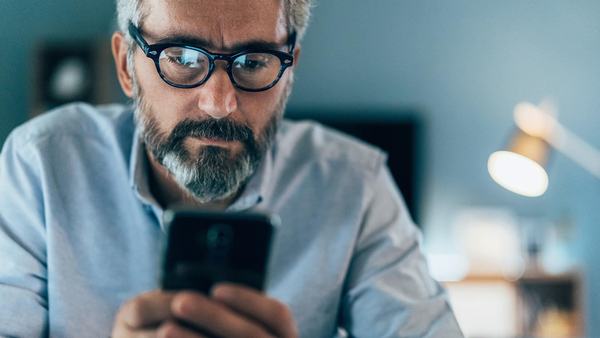 Un uomo con gli occhiali fissa lo smartphone.