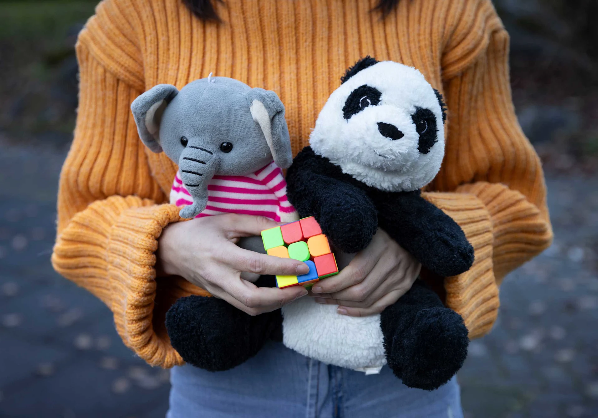 A woman in an orange sweater holds two stuffed animals and a dice in her arms.