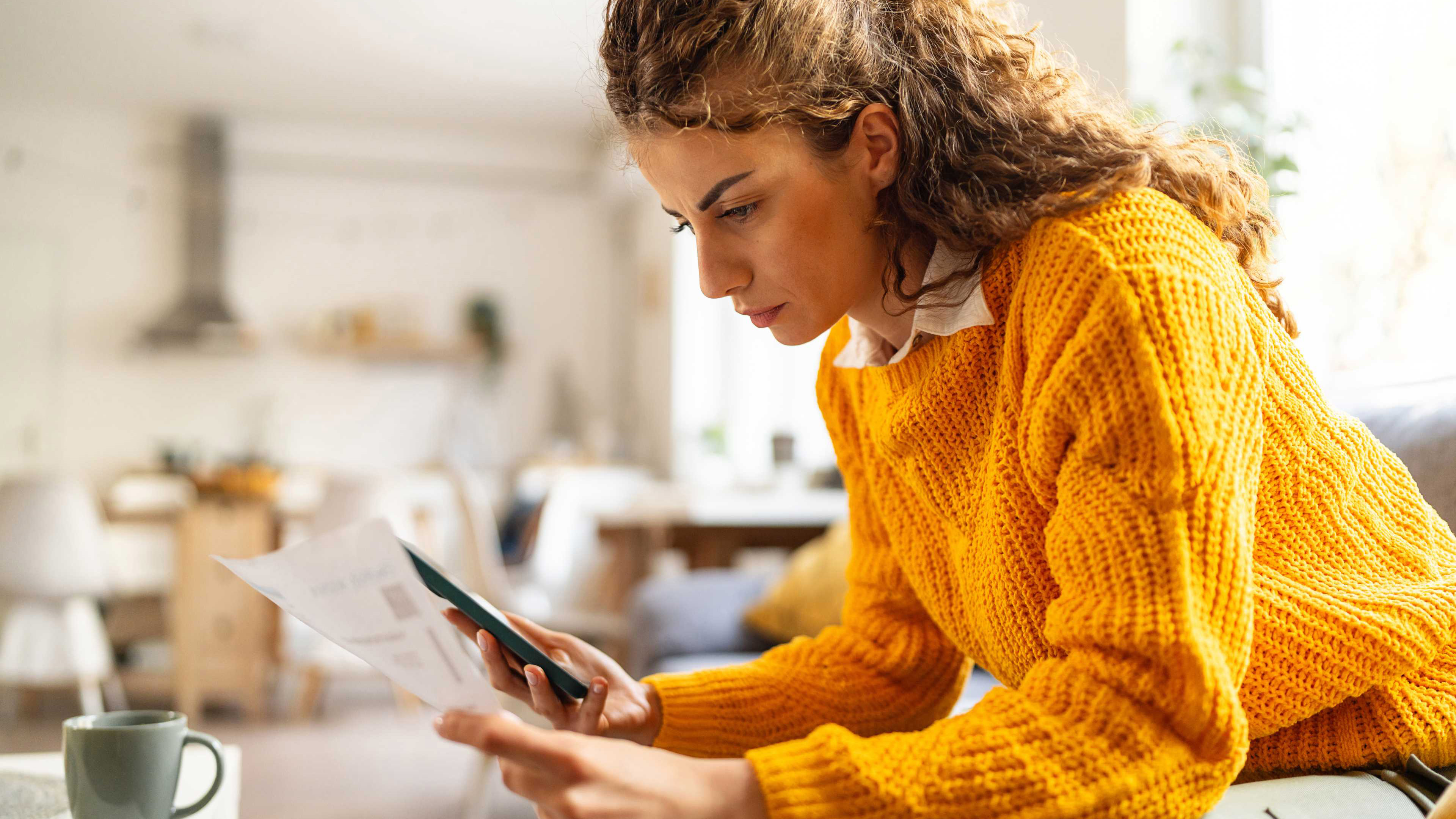 Eine Frau prüft einen Bankauszug und macht Berechnungen auf dem Mobiltelefon