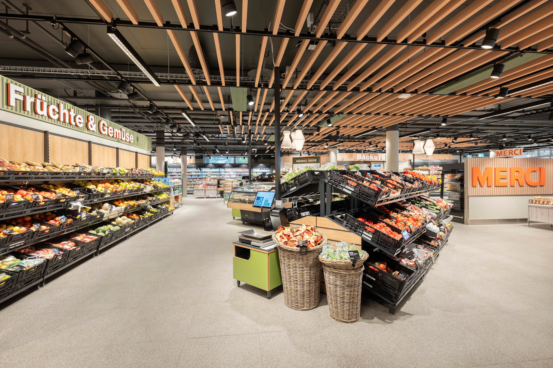 Modern gestalteter Migros‑Supermarkt mit grosszügiger Obst‑ und Gemüseabteilung, übersichtlicher Warenpräsentation und klarer Beschilderung.