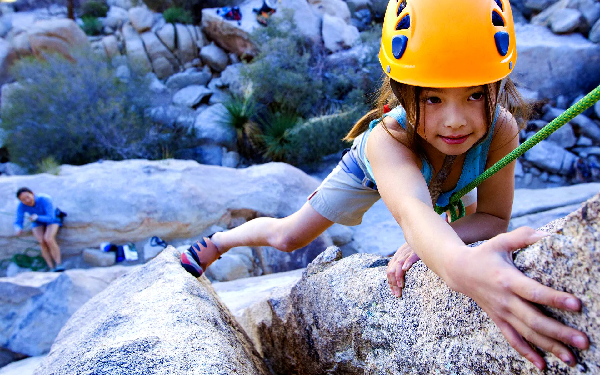Bambina che scala una parete di montagna con casco e corda.