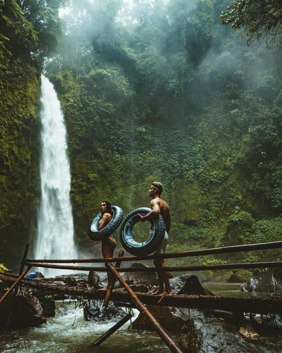 Two Person Carrying Black Inflatable Pool Float on Brown Wooden Bridge Near Waterfalls