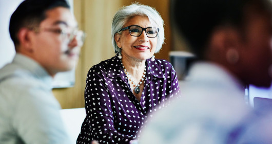 Smiling mature female business owner listening during presentation during meeting in office conference room