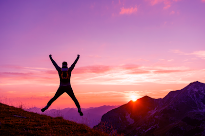 Man on a hike in the mountains jumping at sunset