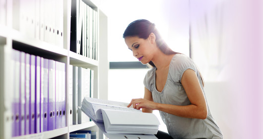 Woman searching through file in front of bookcase of other files