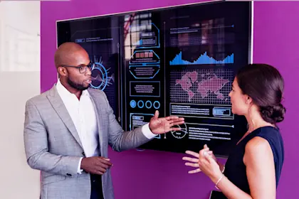 Man and woman discussing graphs on large monitor screen