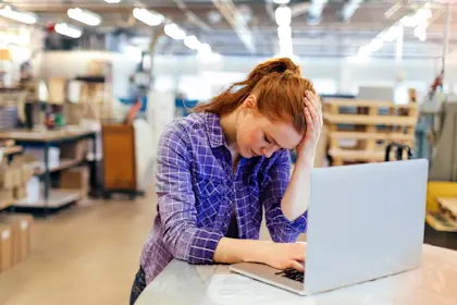 woman sitting at laptop with her hand holding her head