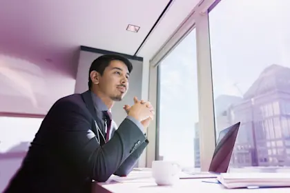 Pensive-businessman-at-laptop-looking-out-urban-office-window_681886833