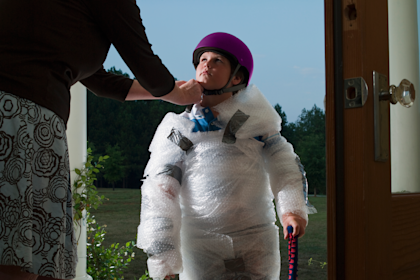 Mom puts helmet on her son's head. He's wrapped in bubble wrap. 