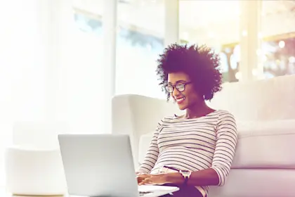 Woman seated at foot of sofa while working on laptop