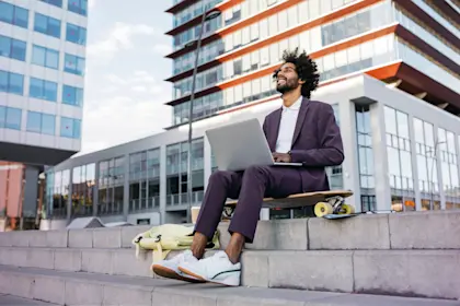 Man sitting on skateboard working on laptop