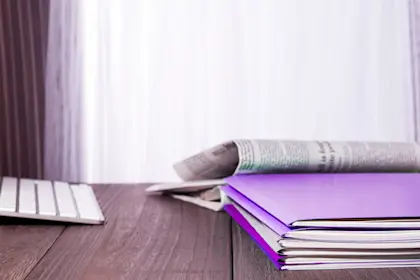 Keyboard, notebooks, and newspaper on wooden desk