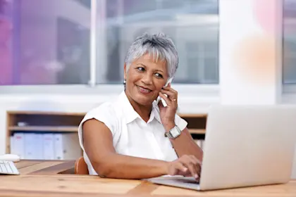mature businesswoman using her cellphone while working on her laptop