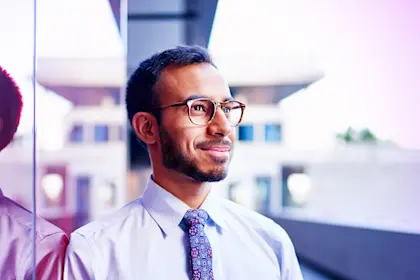 Millenial businessman leaning confidently on a dark glass wall with cityscape background