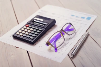 Calculator, pen, eyeglasses and tax forms on wooden table