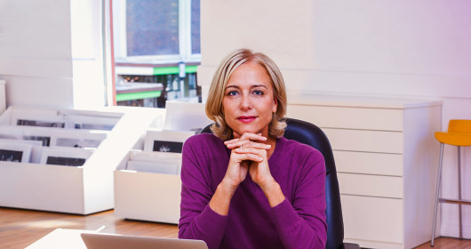 Confident business woman sitting at table resting chin on folded hands