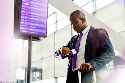 Businessman checks time as he stands below arrival departure board at the airport