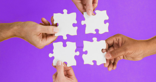 Close up of four hands holding puzzle pieces