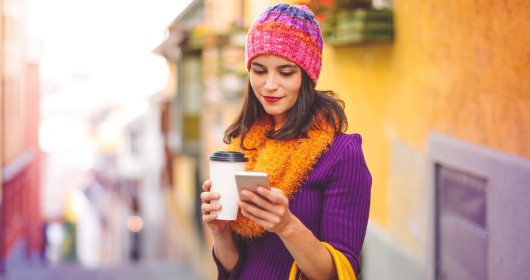 Woman in city holding coffee mug and looking at mobile phone
