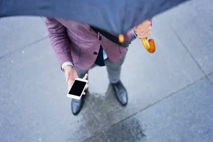 View from above man in purple jacket standing under open umbrella while looking at his phone