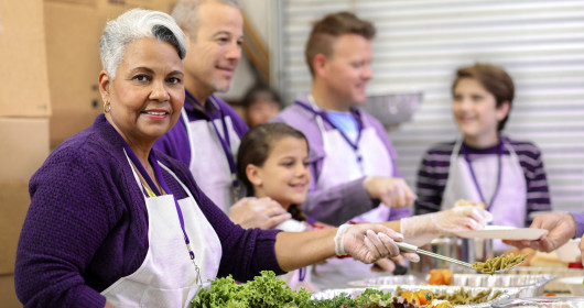 woman smiling while serving food with a group of volunteers at soup kitchen