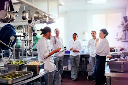 Male check holding digital tablet while talking with staff in kitchen