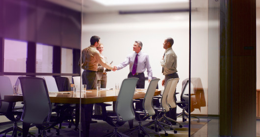 Four businesspeople in boardroom with two shaking hands