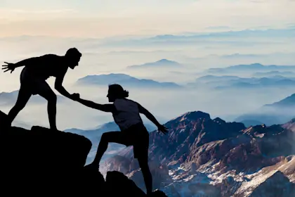 Hikers helping each other climb a mountain