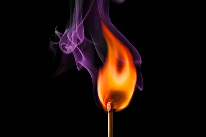 Lit match surrounded in smoke on a dark background