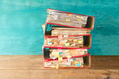 Stack of four messy red binders full of papers