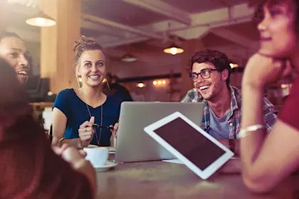 Group of adults sitting around a table with computers and tablet.