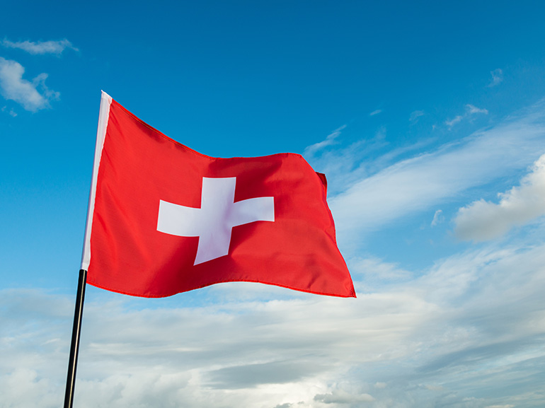 Switzerland's Flag Waving on a Blue and Cloudy Sky Background 