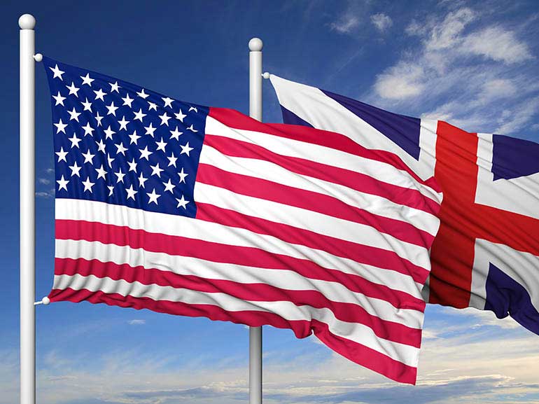 Waving flags of USA and UK on flagpole on blue sky background