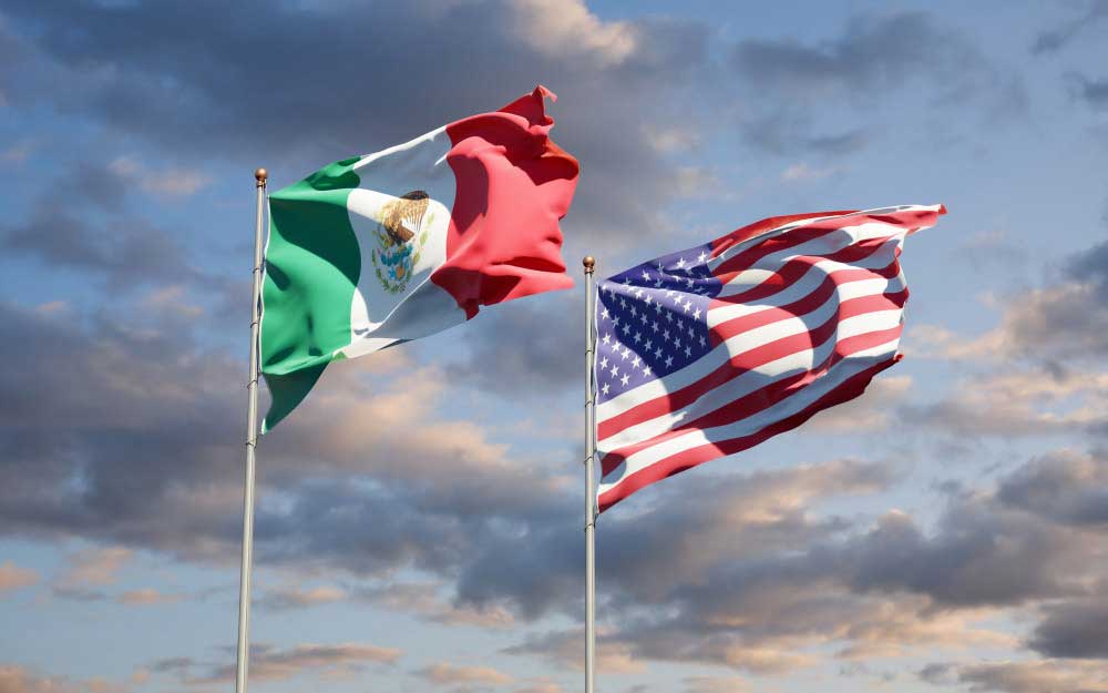 Las banderas de México y EE. UU. una junto a la otra sobre un fondo de cielo nublado