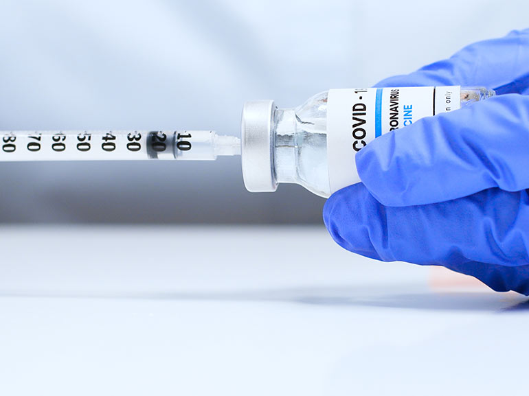 Gloved hand holding a covid-19 vaccine vial and a syringe