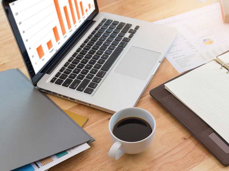 Espacio de trabajo con portátil que muestra gráficos de barras y documentos sobre un escritorio de madera