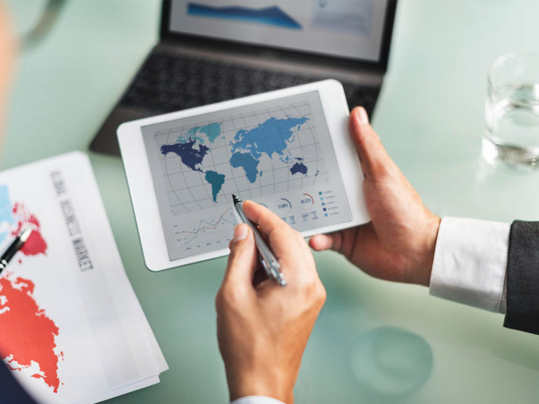 Empresarios con una tableta que muestra un mapa del mundo y datos estadísticos con un ordenador portátil en el fondo