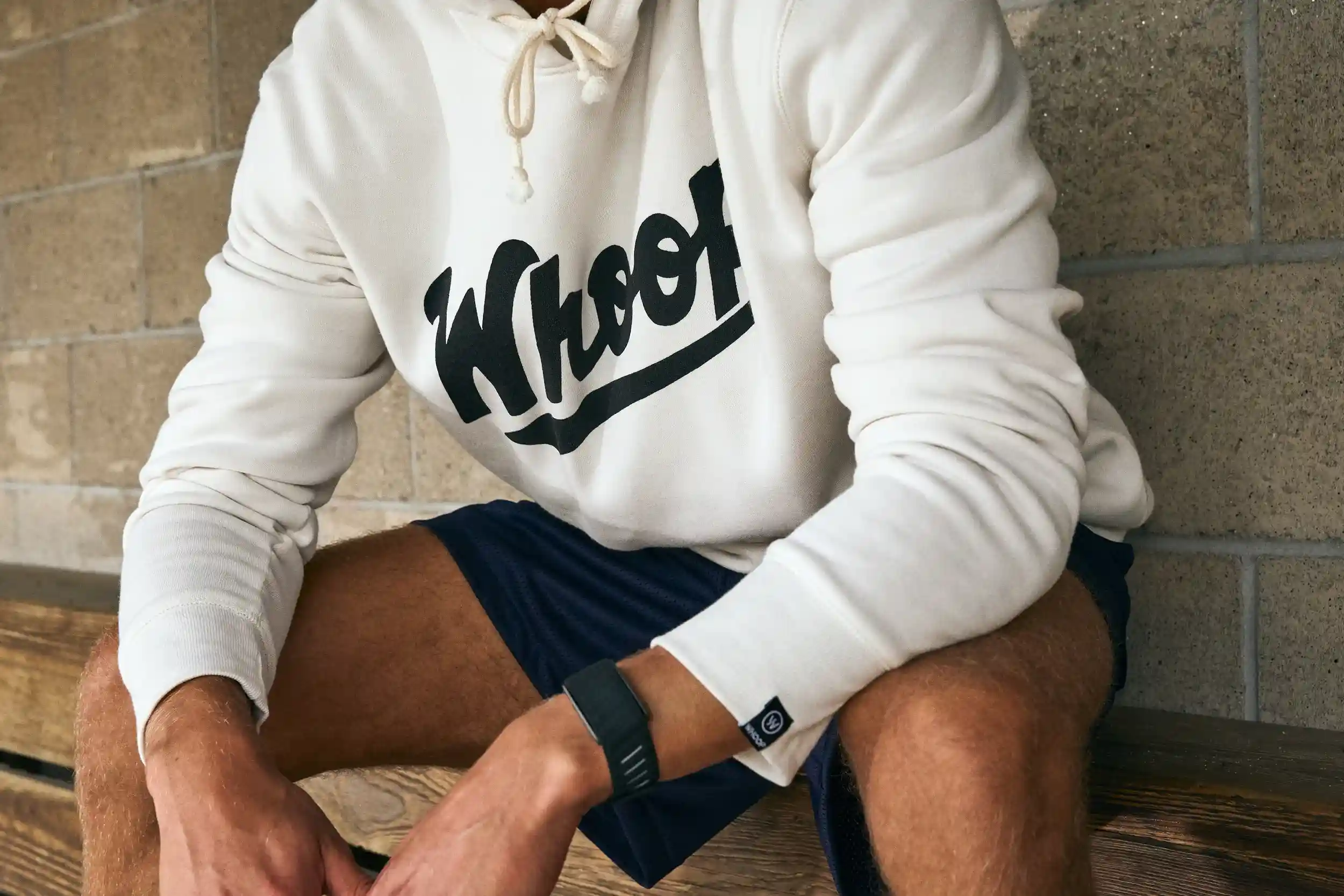 Athlete wearing a WHOOP hoodie and WHOOP wearable while seated on a bench, highlighting performance tracking, recovery monitoring, and everyday athletic lifestyle integration.