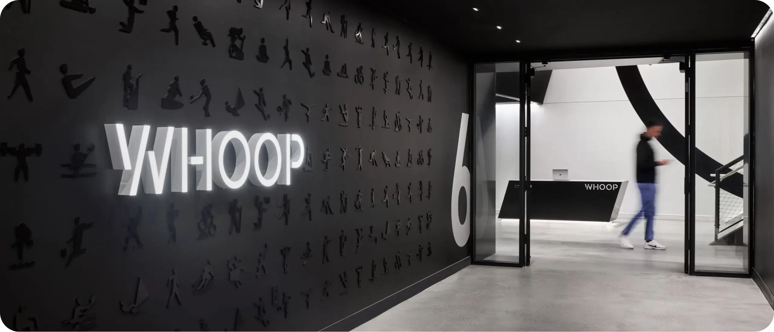 Interior view of the WHOOP office featuring a branded wall with athlete icons and illuminated logo leading into the main entrance.