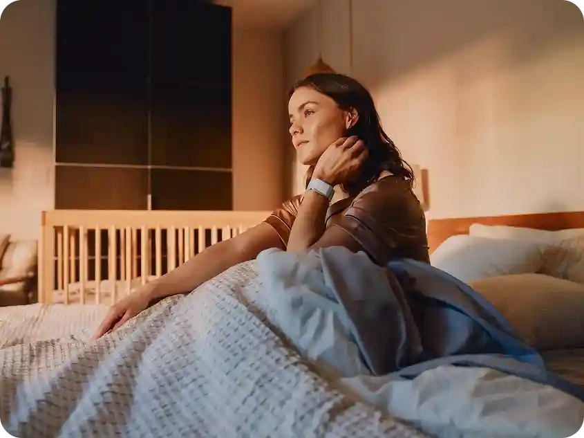 Woman waking up in bed wearing a WHOOP 5.0 band, highlighting morning recovery insights and sleep tracking.