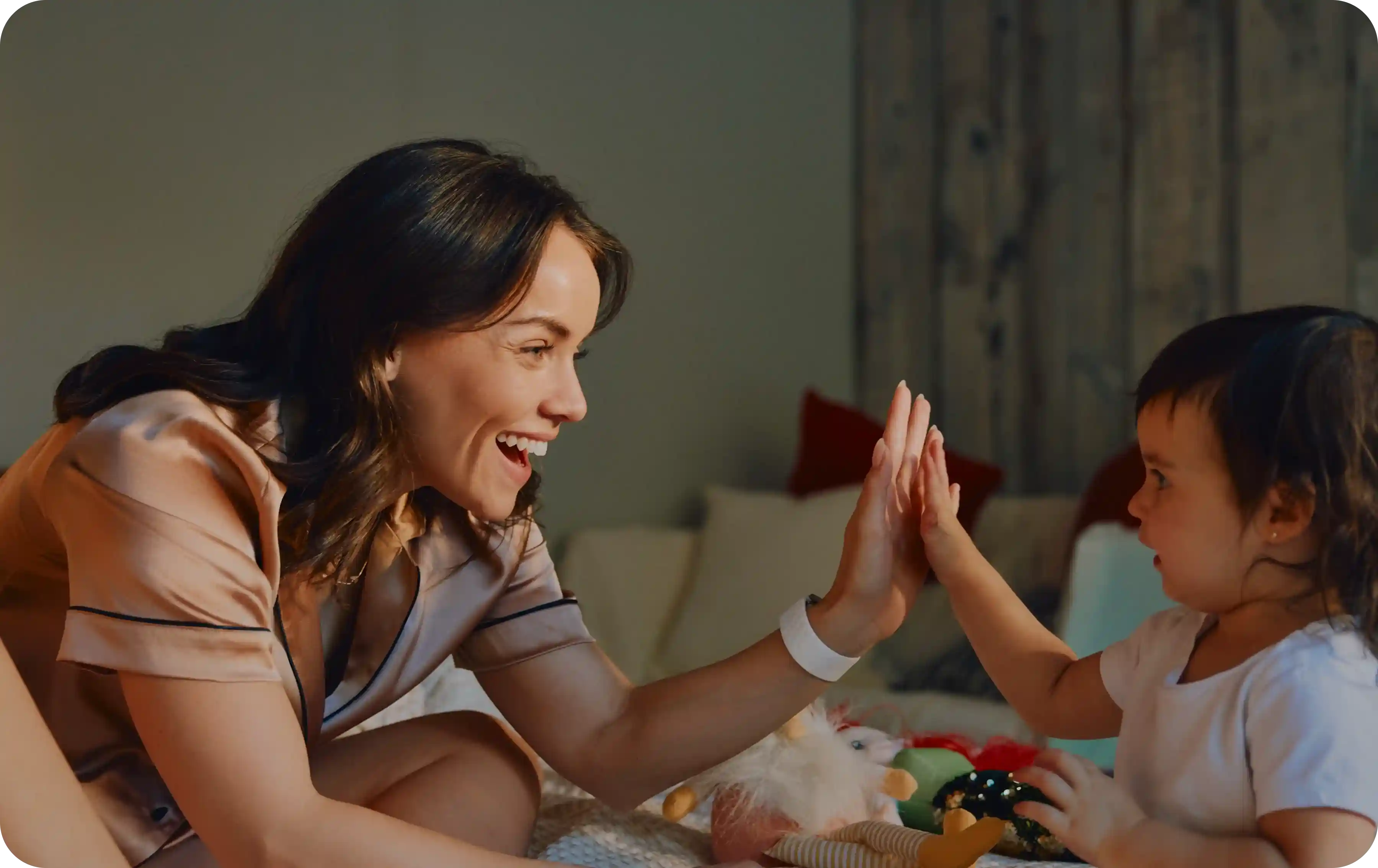 Parent wearing a WHOOP 5.0 band high-fives a toddler on the bed during the evening routine, highlighting continuous sleep, heart rate, HRV, and recovery tracking through family moments.