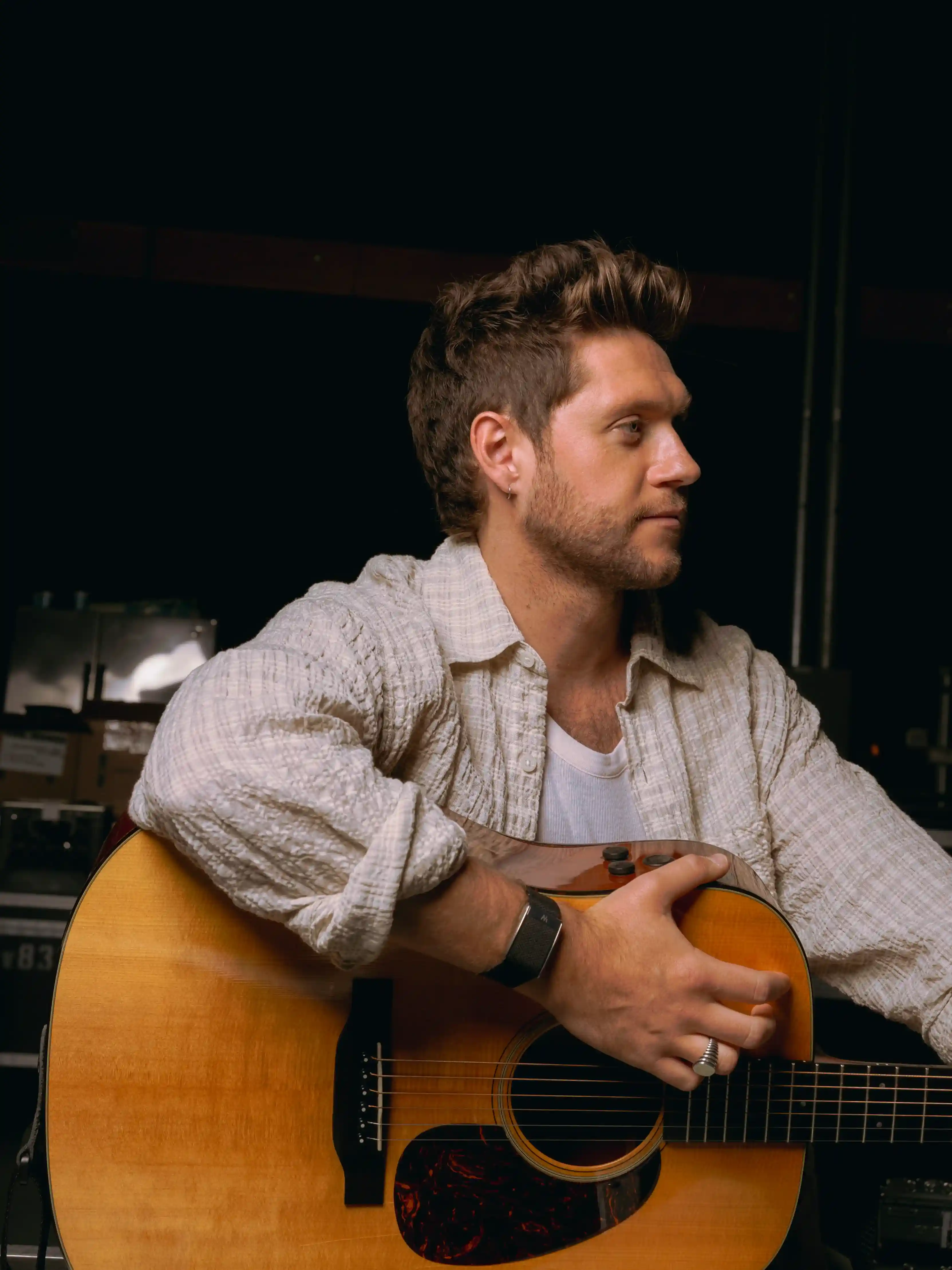 Niall Horan wearing a WHOOP 5.0 band while holding an acoustic guitar backstage, showing recovery and strain tracking for performers.