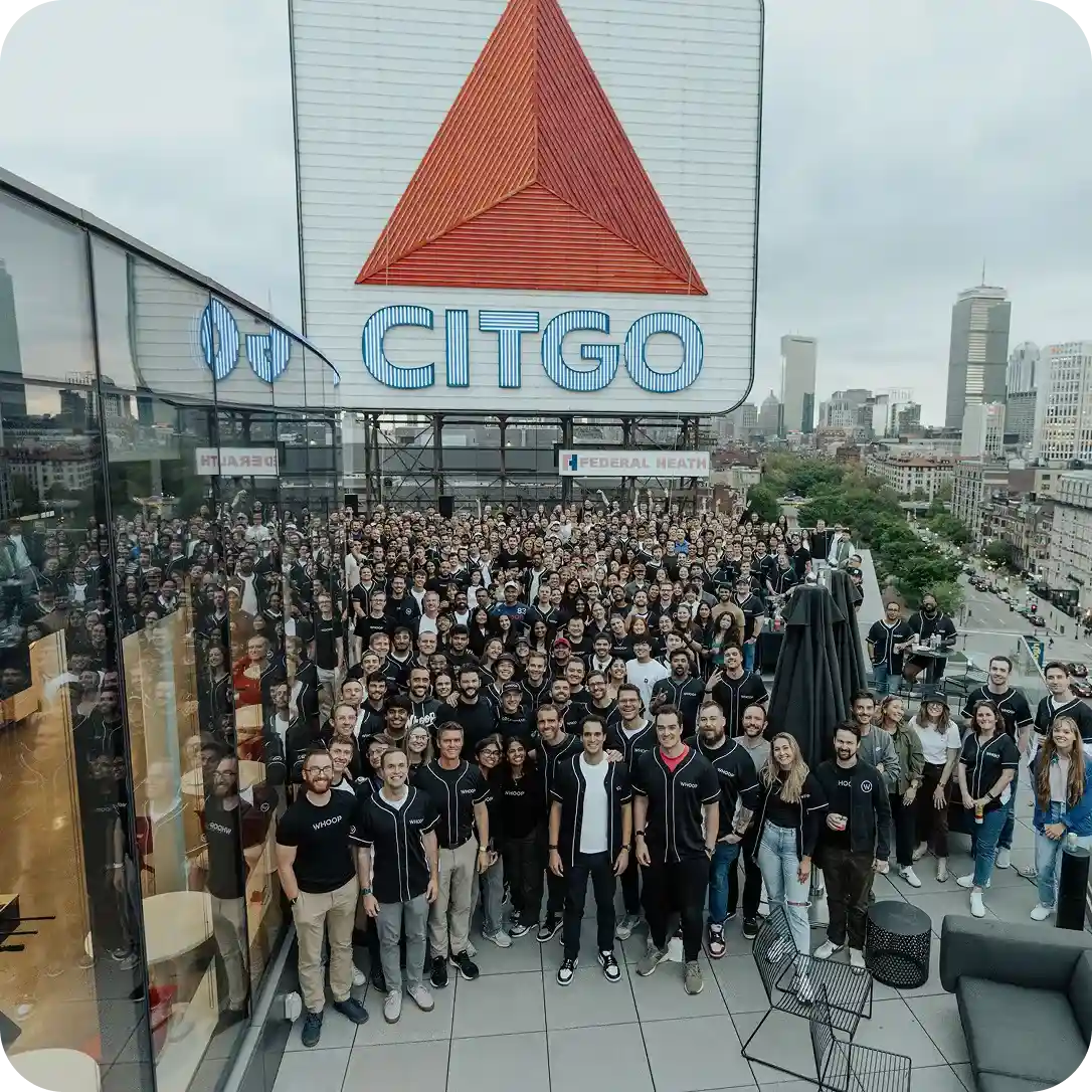 Large group photo of WHOOP team members gathered on a rooftop in Boston beneath the iconic CITGO sign, showcasing company culture and community.