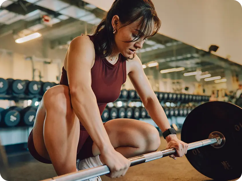 Woman preparing to deadlift while wearing a WHOOP 5.0 band, demonstrating real-time strain tracking during strength training.
