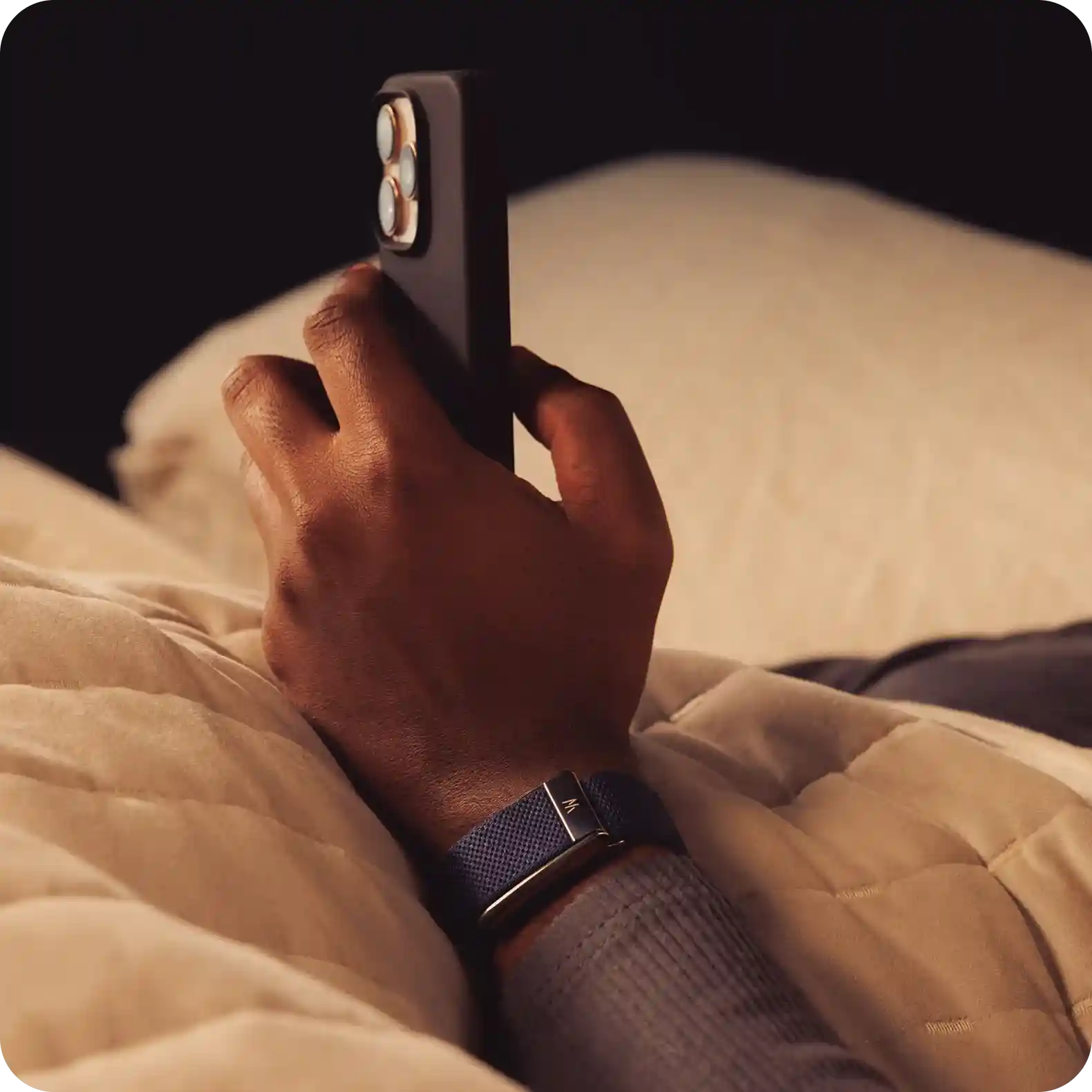 Close-up of a hand wearing a WHOOP 5.0 band while checking a smartphone in bed under a quilt, emphasizing overnight sleep, heart rate, HRV trends, and next-day recovery insights.