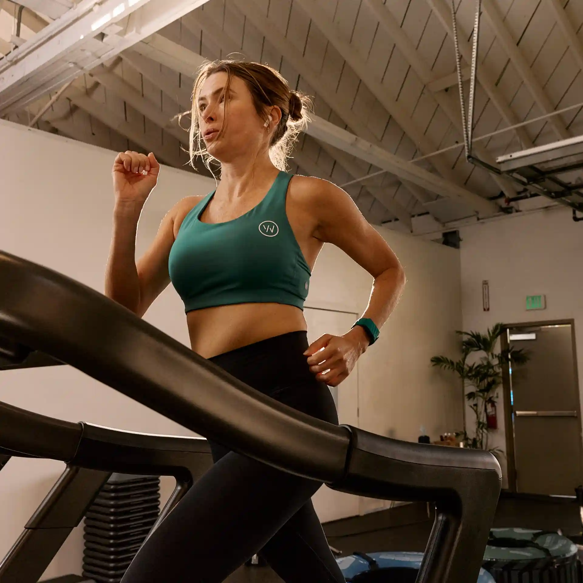 Woman wearing a WHOOP wearable while running on a treadmill, highlighting real-time strain tracking, heart rate monitoring, and performance optimization during indoor training.