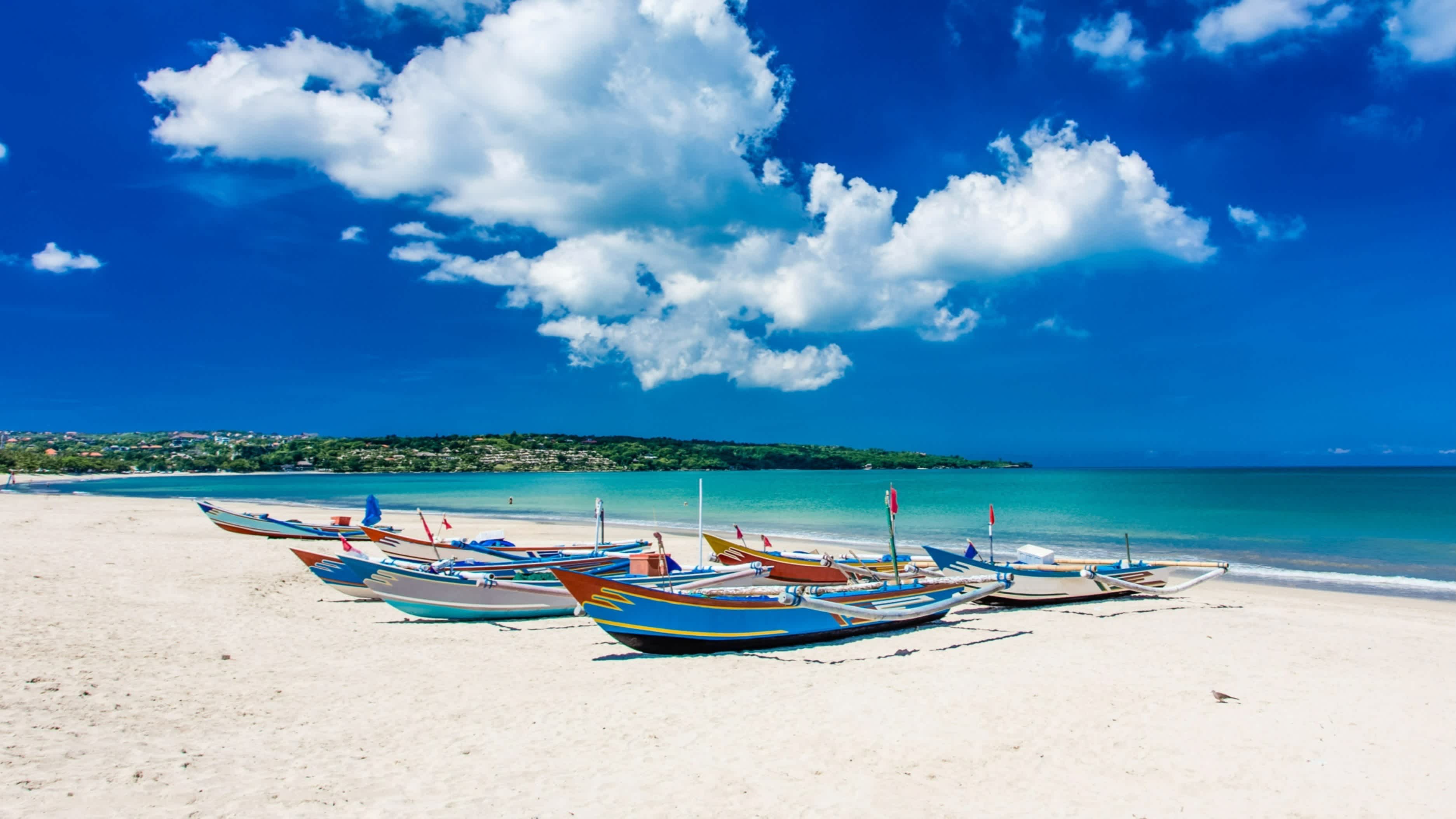 Traditionelle Boote am Sandstrand von Jimbaran, Bali, Indonesia mit Blick auf das Meer sowie einen blauen,wolkigen Himmel und bei Sonnenschein.