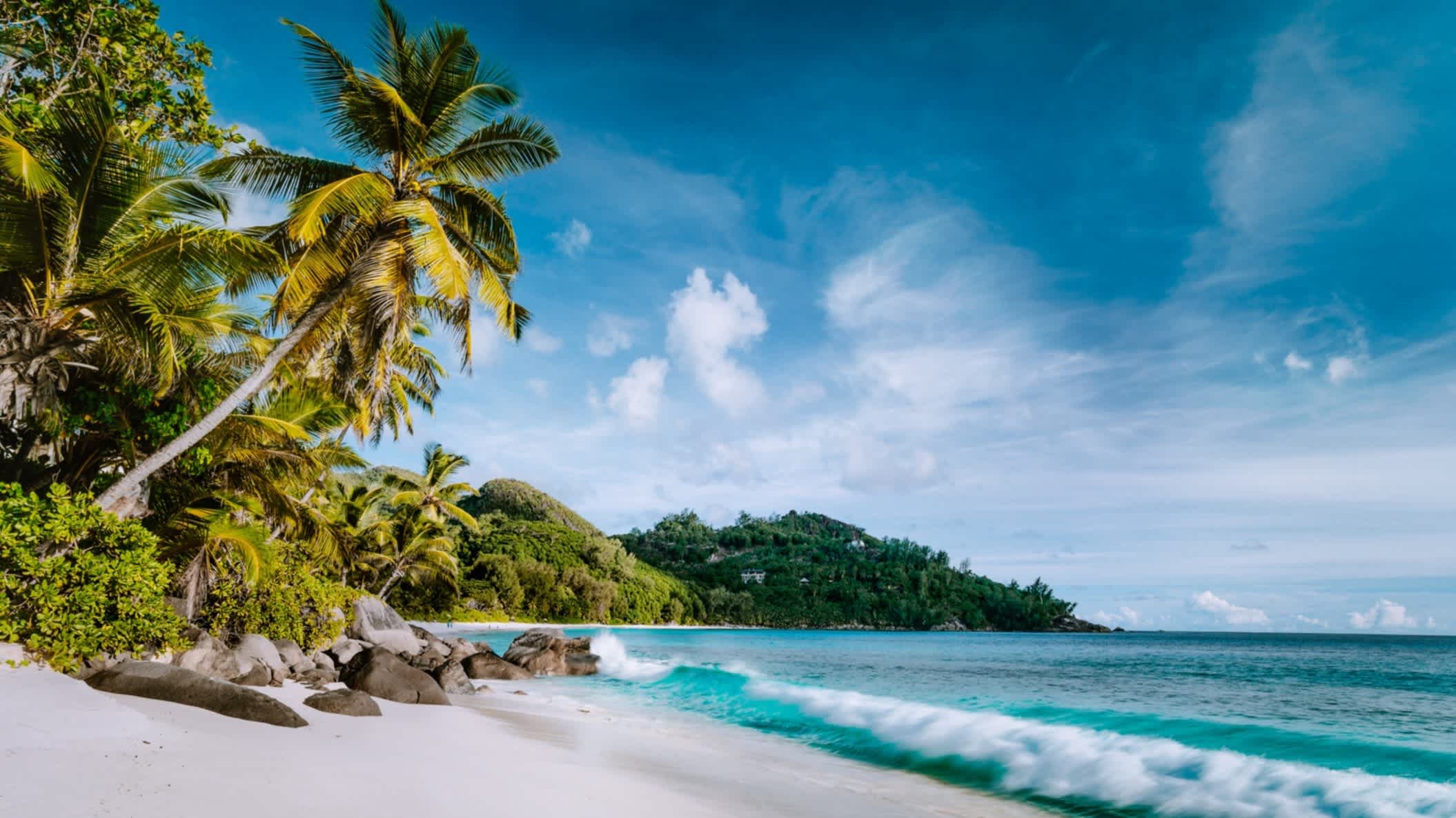 Anse Intendance Strand mit Kokospalmen, weißem Sand, Granitfelsen und blauem, welligem Meer auf der Insel Mahé, Seychellen.